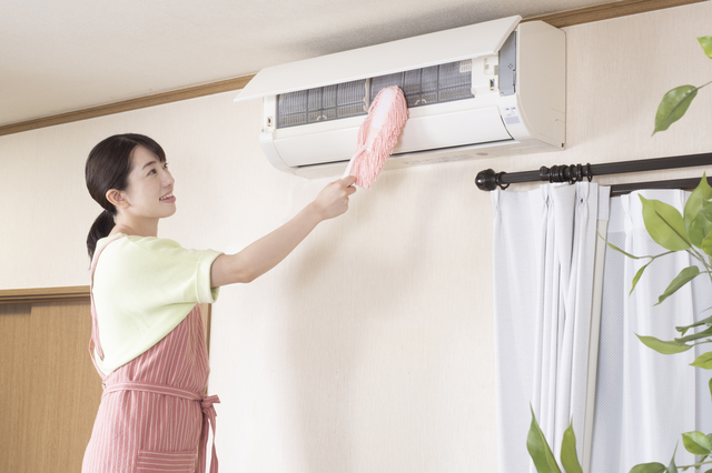電気代を抑えるためにエアコンフィルターの掃除をする女性